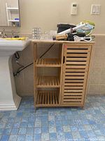 Front view of wood slatted bathroom cabinet with side shelves and various items on top (not included).