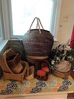 Photo showing multiple baskets including a large lidded woven basket, smaller wicker baskets, and a basket with artificial pumpkins and floral decoration.