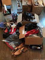 Overview of lot with multiple boxes containing shoes, belts, hair dryers, and shoe stretchers visible on wood floor.