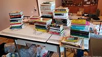 Table with multiple stacks of books arranged in piles, showing a variety of titles and colors indicating different genres including travel, self-help, novels, and non-fiction.