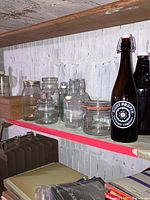 Shelf display showing various clear glass jars and bottles of different sizes with screw and clamp lids, and two large brown glass growlers on the right side.