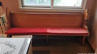 Full view of wooden church pew with red cushions placed under window.
