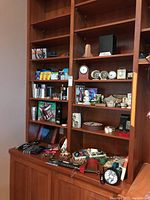 Wide shelf view showing various barware items including metal cocktail shakers, a variety of shelf clocks with analog faces, keychains, buttons, and other small collectibles.
