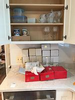 Cabinet with plastic food storage containers, coffee mugs, Mikasa crystal stemware, and glassware boxes on countertop