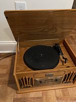 Front angled photo of retro style music center with the top lid open revealing the turntable and tonearm.