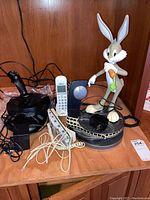 Photo showing entirety of items including Sidewinder joystick, Bugs Bunny animated talking telephone, additional cordless telephones, and cords on wooden shelf.