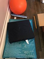 Orange exercise ball, rolled exercise poster on floor, two mats placed on dark wood floor near wall.