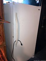 Exterior front view of white upright freezer with handle and power cord.