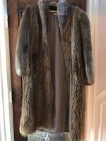 Full frontal view of the long beaver fur coat hanging on a wooden door, showing the full length and fur texture.