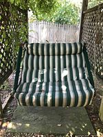 Front view of a cushioned swing with green and white striped fabric showing weathering and some debris on the seat.