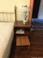 Full view of wooden night stand with table lamp on top and smaller oak table in front