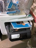 Photo showing HP OfficeJet Pro 8720 printer with paper input tray and some ink cartridges in plastic bags on top.
