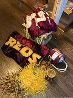 Full lot showing signed jersey draped over box, Redskins pennant, cushions, scarf, yellow pom-pom, plastic helmet, and mug on hardwood floor.