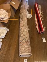 Rug rolled lengthwise on hardwood floor showing overall form and one fringed end