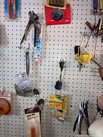 Hand tools including pliers, fan oil container, small hardware items, and packaged hooks on pegboard