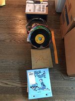 Overhead view showing stacked vinyl 45 records, Rhythm Tote record carrier, and Glenn Miller album box on wood floor.