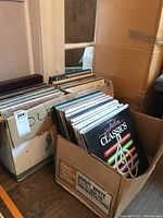 Photo showing multiple cardboard boxes filled with dozens of vinyl records, with visible album covers including Hooked on Classics