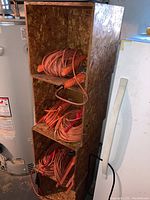 A tall handmade wood box shelf containing multiple orange extension cords coiled on black keepers.