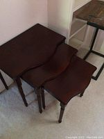 Three cherry wood nesting tables stacked inside each other showing different sizes, legs, and curved edges