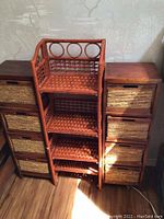 Front view of three storage towers: two wooden framed towers with wicker basket drawers flanking a reddish wicker shelving tower with decorative circular top.