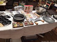 Full view of various baking items on table including pans, whisks, rolling pins, cupcake decorating set, cooling racks