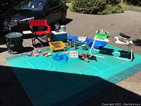 Overview of all camping items arranged on green outdoor mat under sunlight
