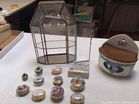 Wide view of all items on table including glass display case, enamel boxes, vintage salt container, and toothpaste box.