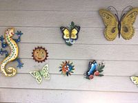 Photo showing multiple metal butterflies, suns, and a yellow metal gecko on a light grey wall