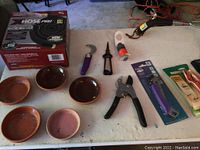 Photo of pruning shears, hose in box, plastic plant saucers and other hand tools on table.