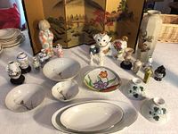 Wide view of all items presented together on white tablecloth including plates, bowls, figurines, vases, and screen