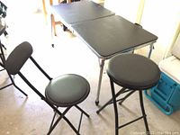 Two small black folding chairs and small round folding table grouped with large rectangular folding table