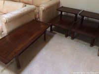 Overall view of the three-piece set including two end tables and coffee table made of cherry wood with brass trim.
