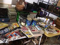 Overview of paint supplies including paint cans, brushes, rollers, and accessories laid out on tables and shelves.