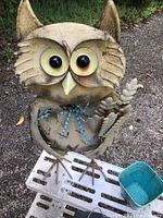Close-up of large metal owl yard art with detailed eyes and holding a branch