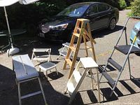 All items displayed outdoors on driveway including wooden step ladders, folding step stools, and aluminum workbench.