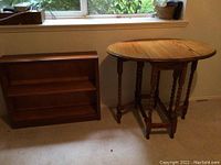 Photo showing the vintage drop leaf table and the small bookshelf side by side near a window, highlighting the wood finishes and shapes.