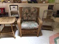 Full view of cushioned wicker armchair with wide arms, side table, and metal stand with dome.