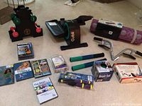 Full display of all workout equipment including Cubii elliptical, hand weights on stand, exercise mat, resistance bars, weight ball, Pilates yoga kit, jump rope, and workout DVDs.