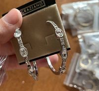 Close-up of a pair of silver-tone hoop earrings with multiple clear crystal stones in oval and rectangular shapes on R.J. Graziano branded card