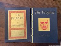 Two ornate hardcover copies of The Prophet by Kahlil Gibran shown side by side on a wooden surface, one with gold face illustration and Japanese-style spine binding.