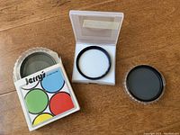 Top view with multiple 58mm filters including red, green, yellow, blue colored filters in Jerry's branded holder, one neutral or UV filter in a plastic case, and a dark circular filter in a separate plastic container.