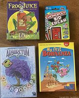 Top view of four card game boxes: Frog Juice, Monopoly Bid England, Arboretum, and My First Bohnanza