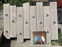Wooden hanging display board with metal clips, displayed outdoors with bird art plaque in front