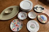 Various round plates and serving dishes including an Umbra eye-shaped ceramic serving plate and dish, white dinner plates, themed decorative plates.