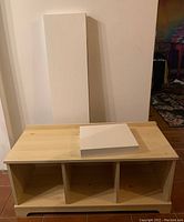 Birch veneer storage bench showing three open cubby compartments and natural wood finish top with some water damage.