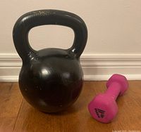 Photo of black 24kg kettlebell and pink 5lb dumbbell side by side on wooden floor
