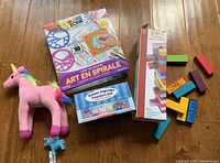 Overview photo of all items: spiral art kit, cupcake counters set box, wooden puzzle blocks, pink unicorn plush and small unicorn figurine.