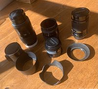 Overview of multiple Minolta lenses and lens hoods placed on wooden surface to show lot contents.