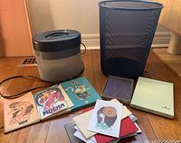 Compact electric paper shredder, black and grey, with power cord shown next to stationary and trash can