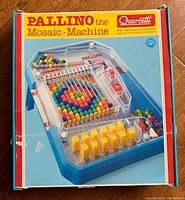 Closed box of the Quercetti Pallino Mosaic Machine game showing the product photo on the lid with multicolored balls inside the game unit and branding details.